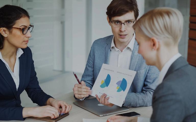 Ein Team im Büro bespricht Vertriebszahlen an einem Bildschirm mit Diagrammen