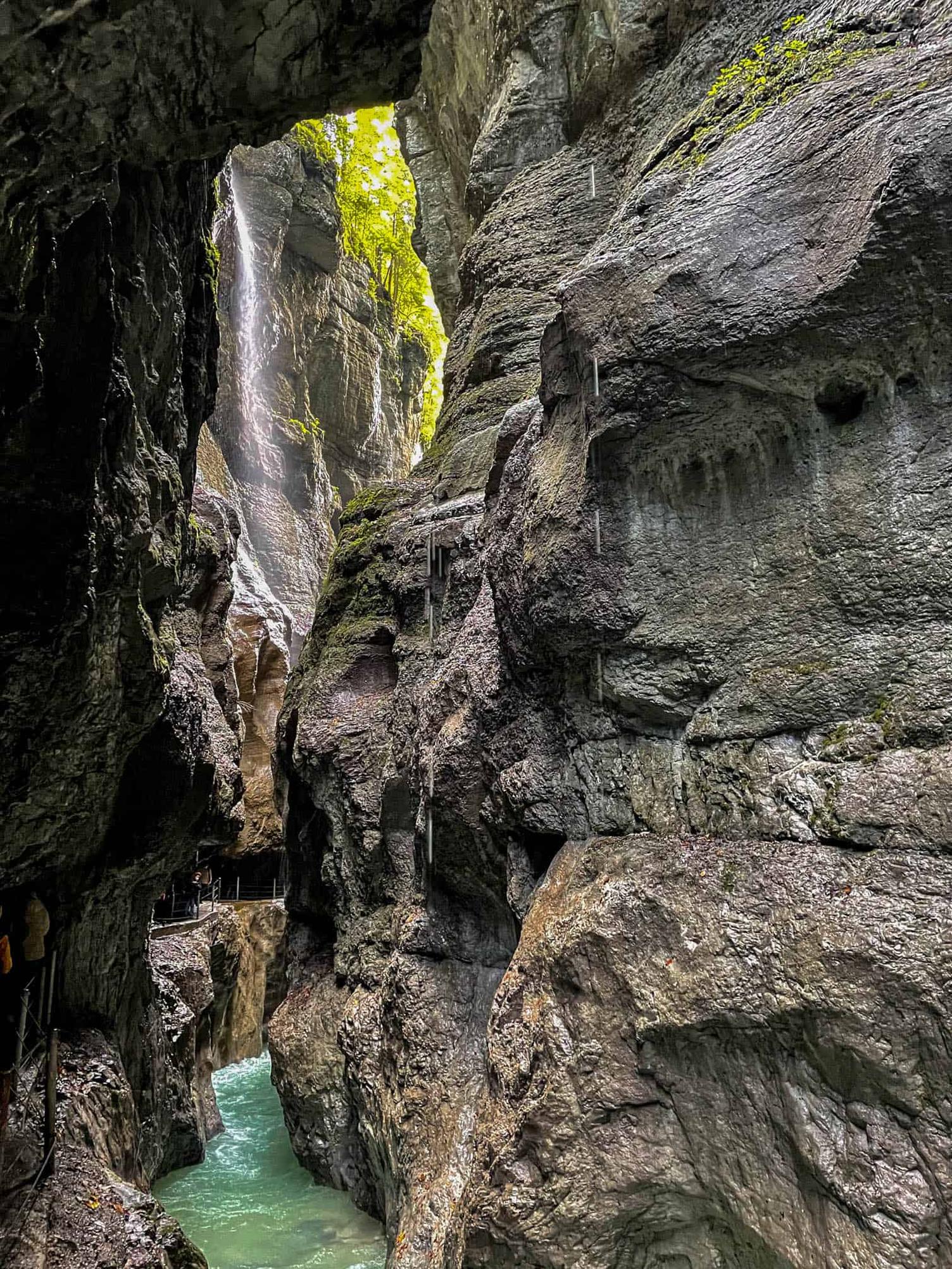 Foto einer engen Felsschlucht mit Wasserfall, unten führt ein schmaler Steg am türkisfarbenen Wasser entlang