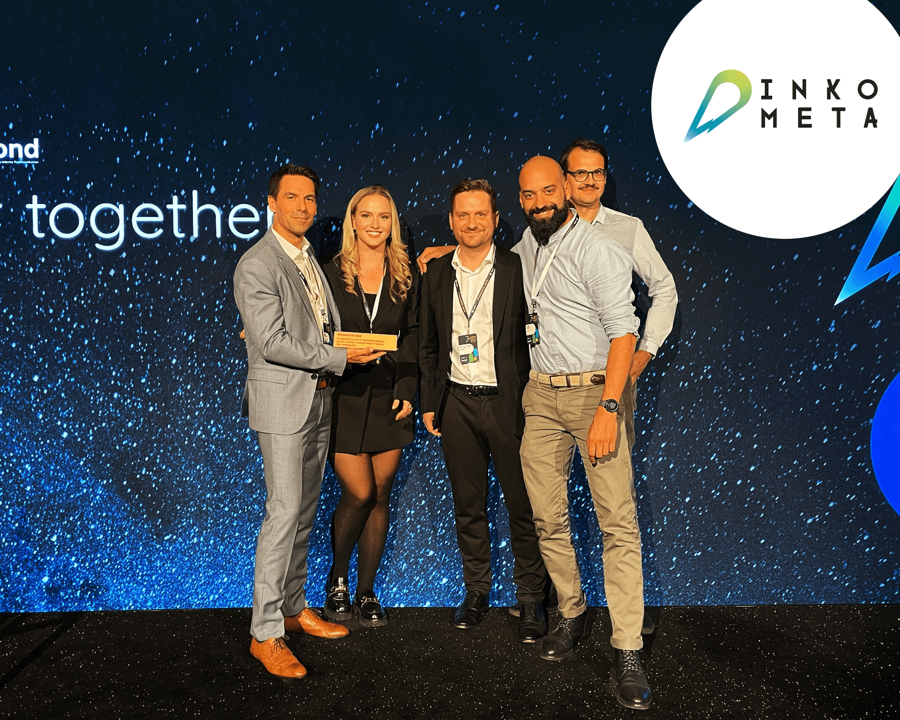Fünf Personen in Business-Kleidung halten einen Inkometa-Award vor einer blauen Event-Bühne mit Inkometa-Logo.
