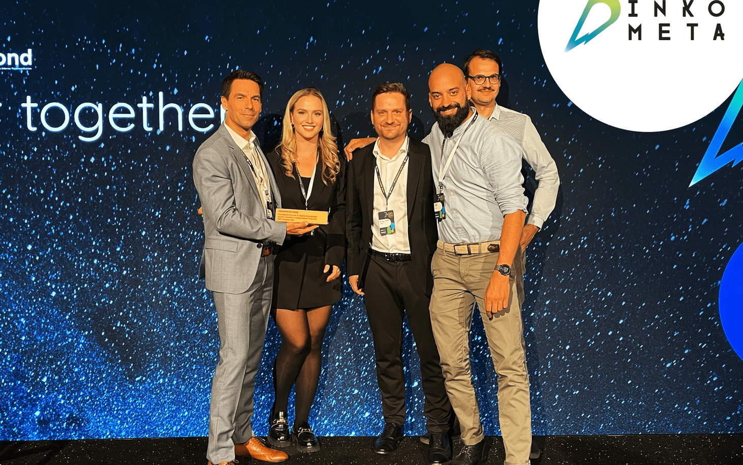 Fünf Personen in Business-Kleidung halten einen Inkometa-Award vor einer blauen Event-Bühne mit Inkometa-Logo.
