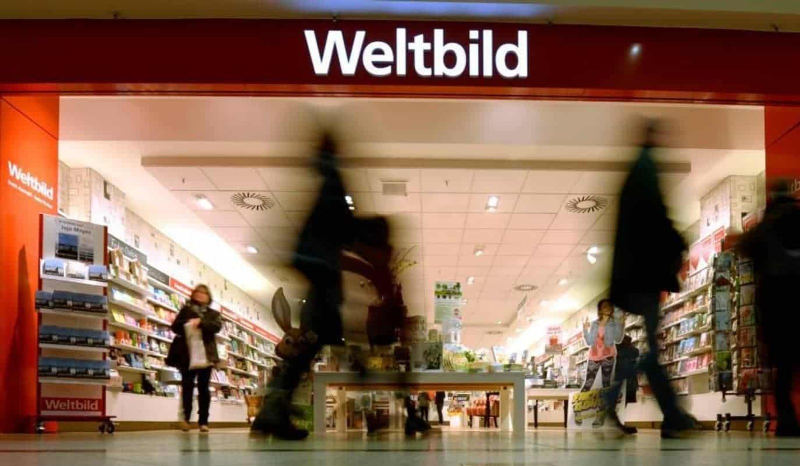 Eingang einer Weltbild-Filiale in einem Einkaufszentrum, Kundschaft läuft an gefüllten Bücher- und Zeitschriftenregalen vorbei