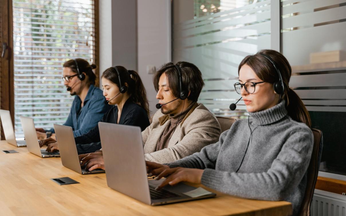 Ein Service-Team arbeitet mit Laptops und Headsets in einem modernen Büro