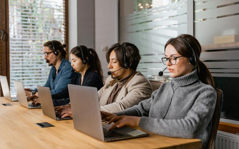 Ein Service-Team arbeitet mit Laptops und Headsets in einem modernen Büro