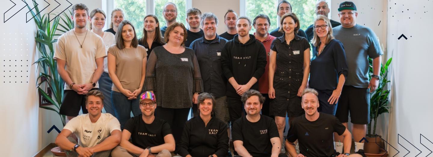 Gruppenfoto von etwa zwanzig Personen in zwei Reihen in einem hellen Innenraum, viele mit Shirts mit dem Schriftzug TEAM XALT