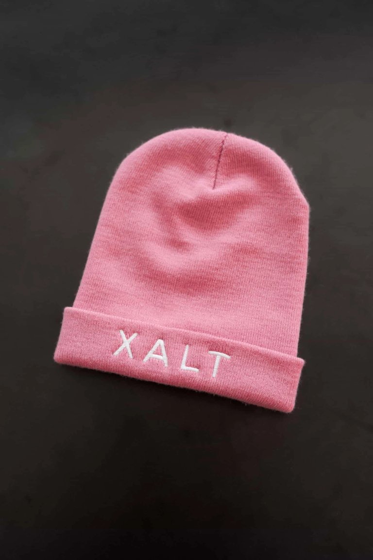Eine rosa Strickmütze mit weißer XALT-Stickerei am Bund