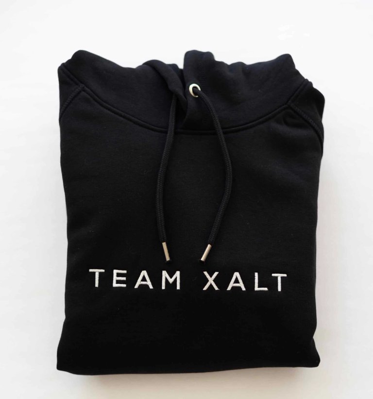 Ein gefalteter schwarzer Kapuzenpullover mit weißer TEAM-XALT-Stickerei
