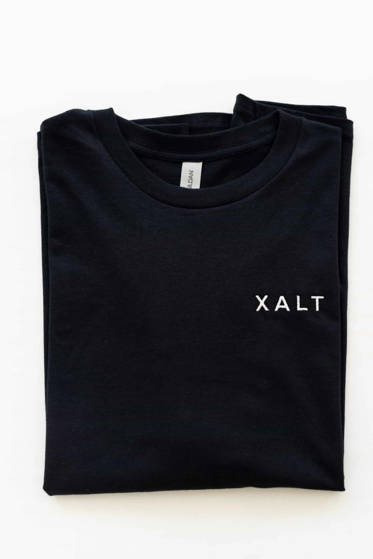 Ein gefaltetes schwarzes T-Shirt mit weißem XALT-Schriftzug auf der Brust
