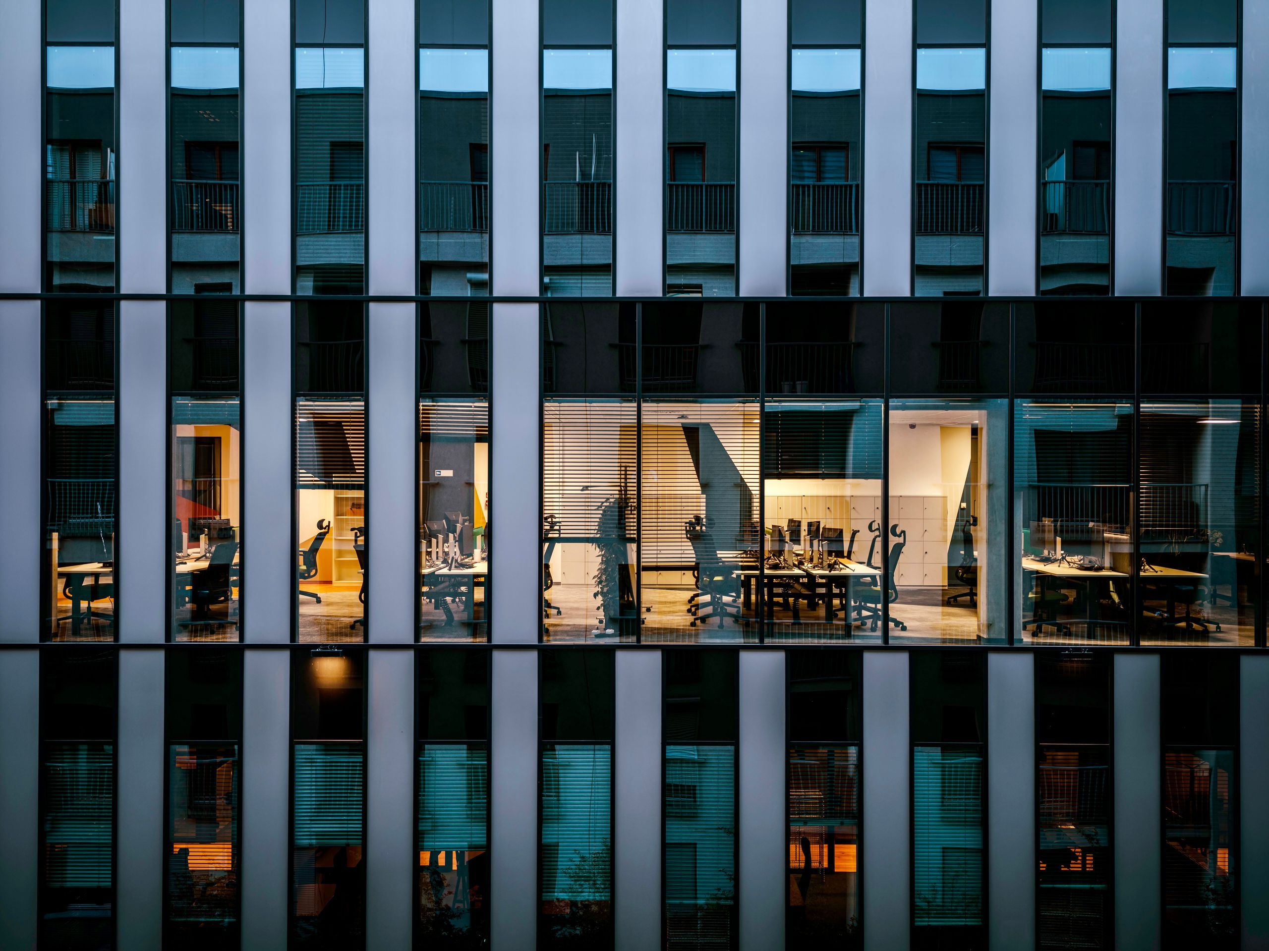 Glass facade of an office building in the evening, one floor with lit workstations
