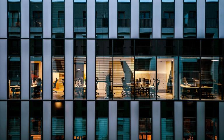 Glass facade of an office building in the evening, one floor with lit workstations