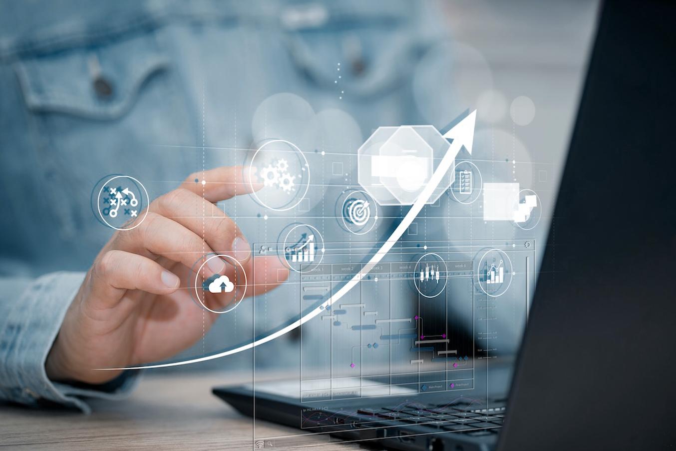 A person touches a floating interface with charts, icons and a bar-chart schedule above a laptop