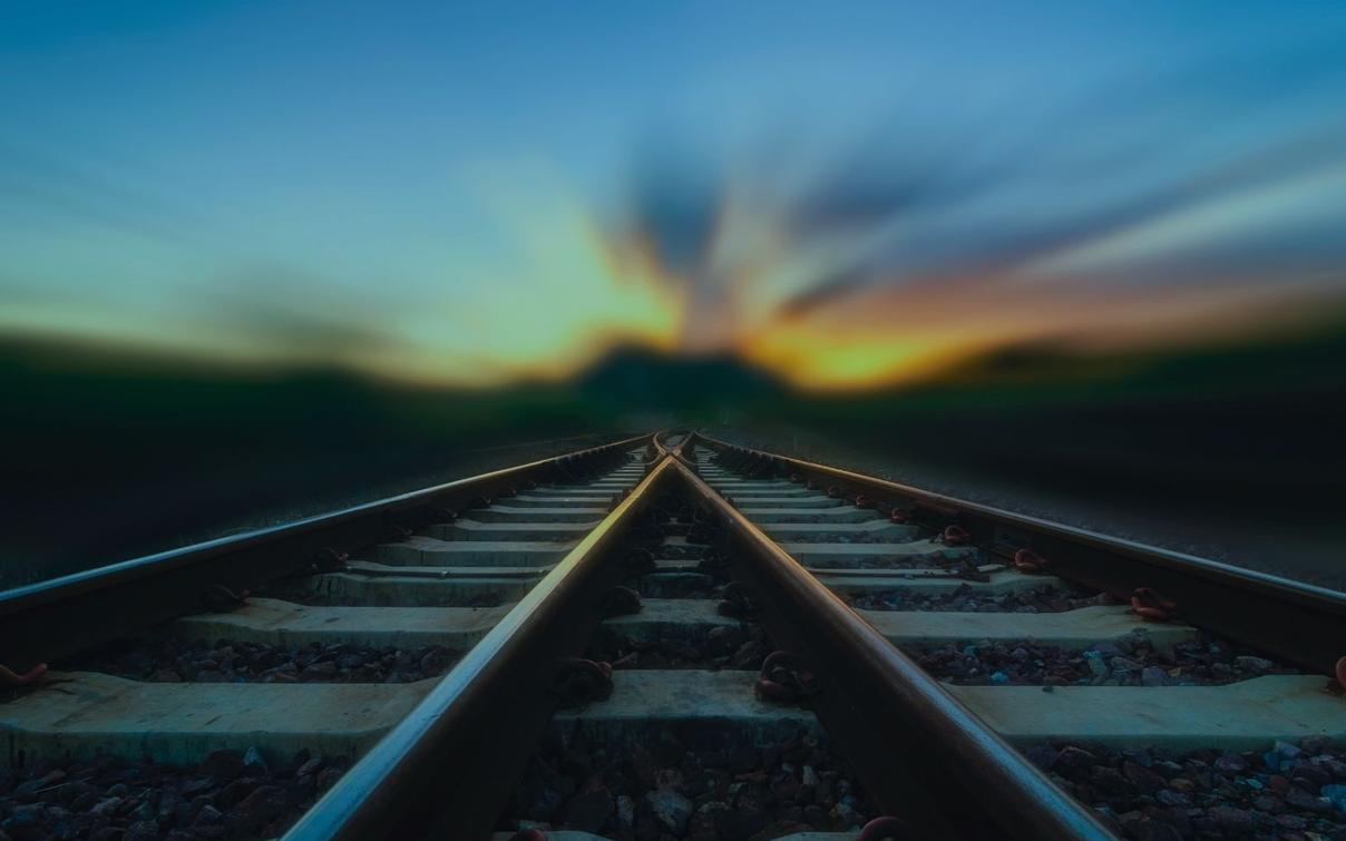 Eisenbahnschienen, die sich in der Ferne gabeln, bei Sonnenuntergang mit verschwommenem Himmel.