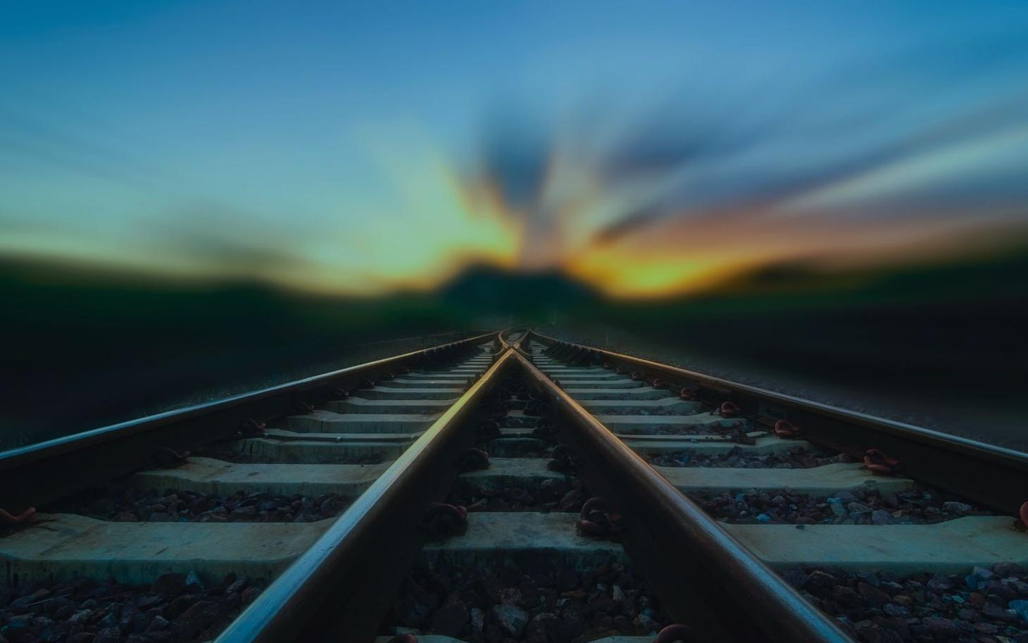 Eisenbahnschienen, die sich in der Ferne gabeln, bei Sonnenuntergang mit verschwommenem Himmel.