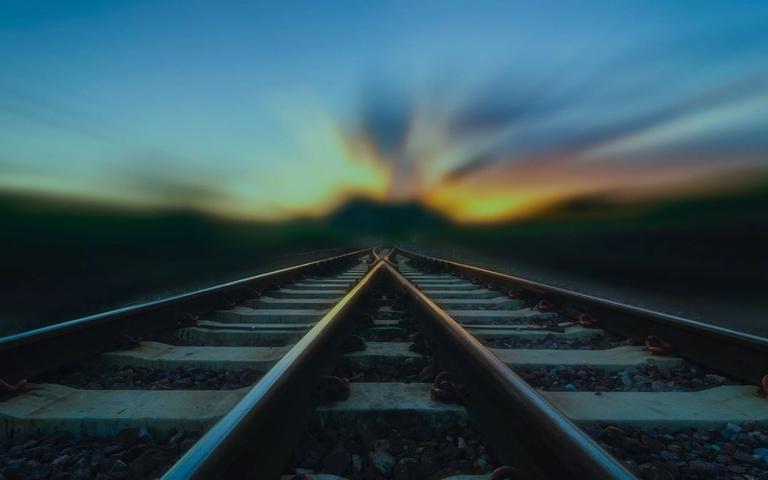 Eisenbahnschienen, die sich in der Ferne gabeln, bei Sonnenuntergang mit verschwommenem Himmel.