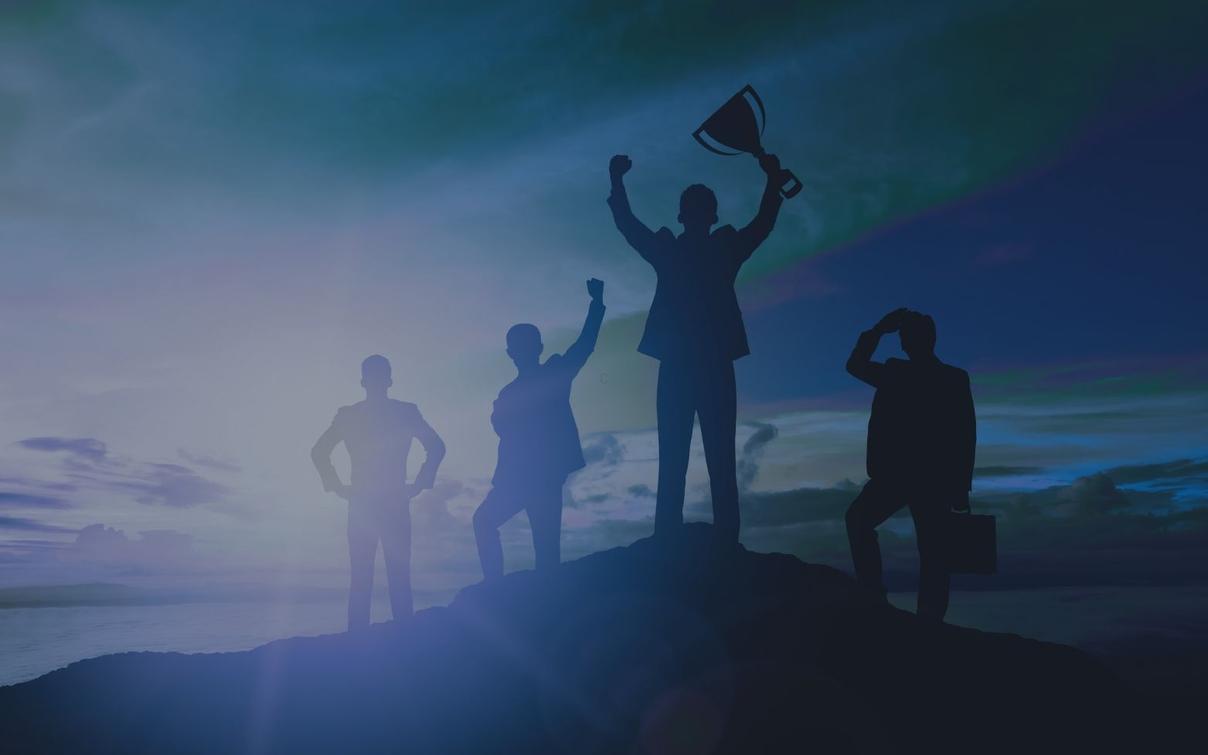 Silhouetten von vier Geschäftsleuten auf einem Berggipfel, einer hält einen Pokal in die Höhe vor blauem Himmel.