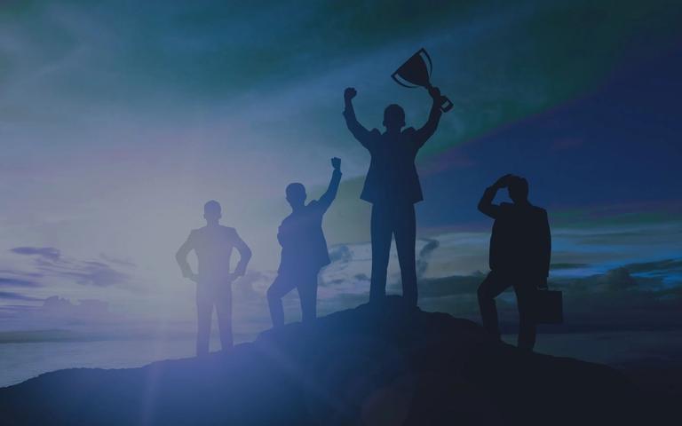 Silhouetten von vier Geschäftsleuten auf einem Berggipfel, einer hält einen Pokal in die Höhe vor blauem Himmel.