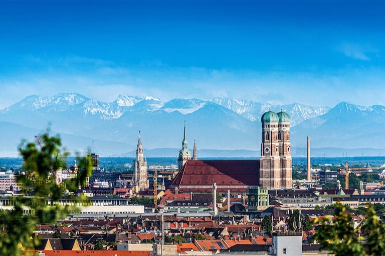 Eine Stadtansicht von München mit roten Dächern und den grünen Kuppeln der Frauenkirche