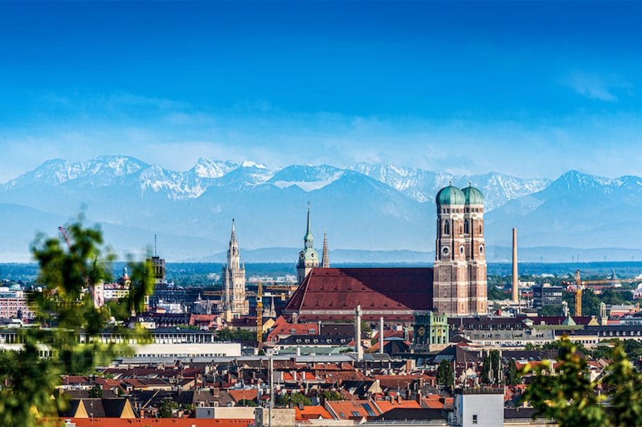 Eine Stadtansicht von München mit roten Dächern und den grünen Kuppeln der Frauenkirche