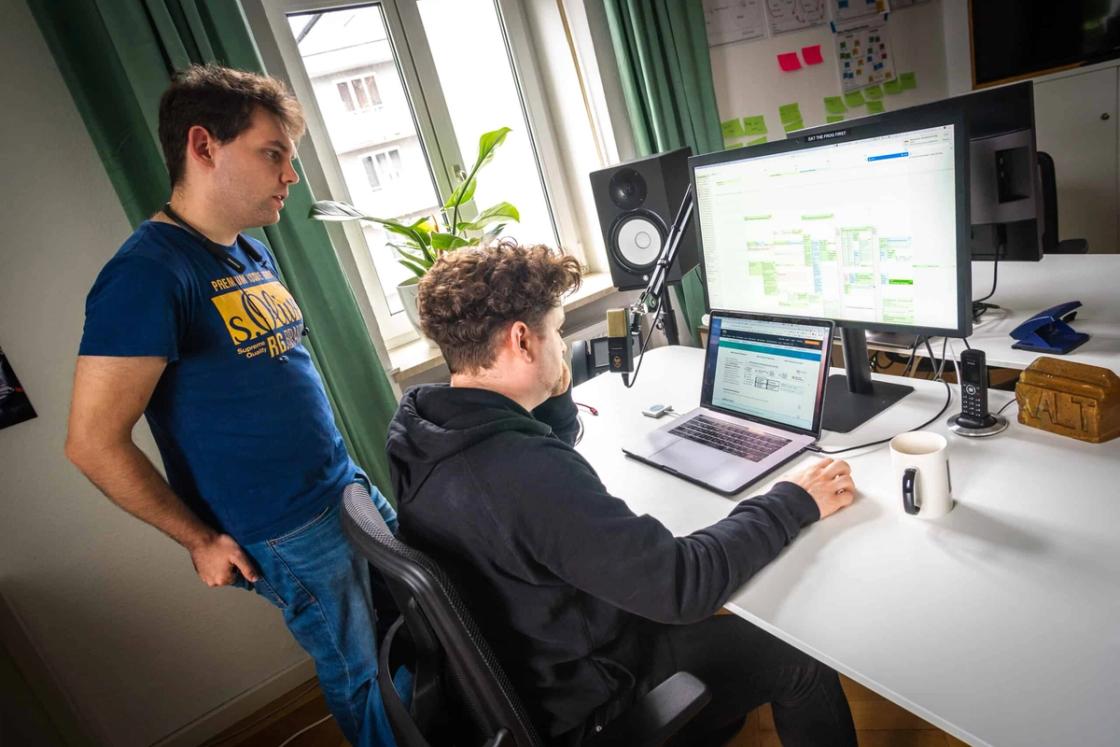 Zwei Männer arbeiten im Büro an einem Schreibtisch mit Laptop und Monitor