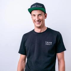 Ein lächelnder Mann mit schwarzer Kappe und TEAM-XALT-Shirt vor hellem Hintergrund