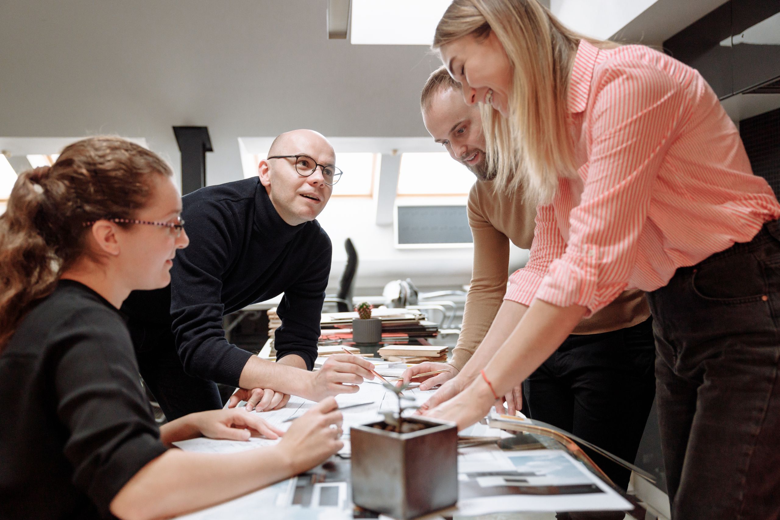 Four colleagues lean over documents together at an office table