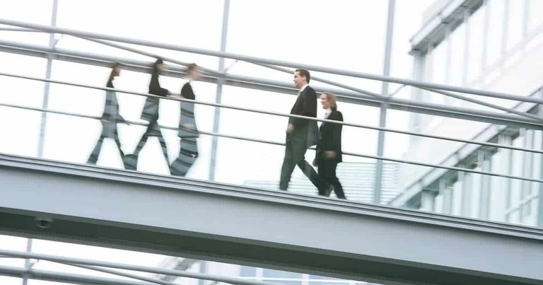 Mehrere Personen in Geschaeftskleidung gehen ueber eine ueberdachte Fussgaengerbruecke