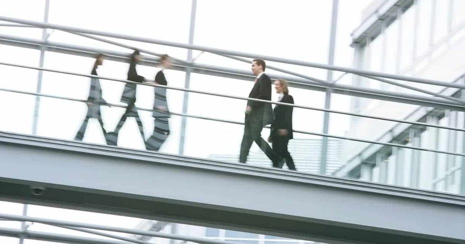 Mehrere Personen in Geschaeftskleidung gehen ueber eine ueberdachte Fussgaengerbruecke