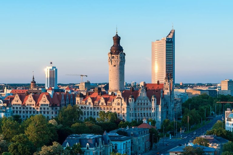 Eine Stadtansicht von Leipzig mit dem spitzen Turm des Neuen Rathauses, roten Ziegeldächern und Hochhäusern im Hintergrund