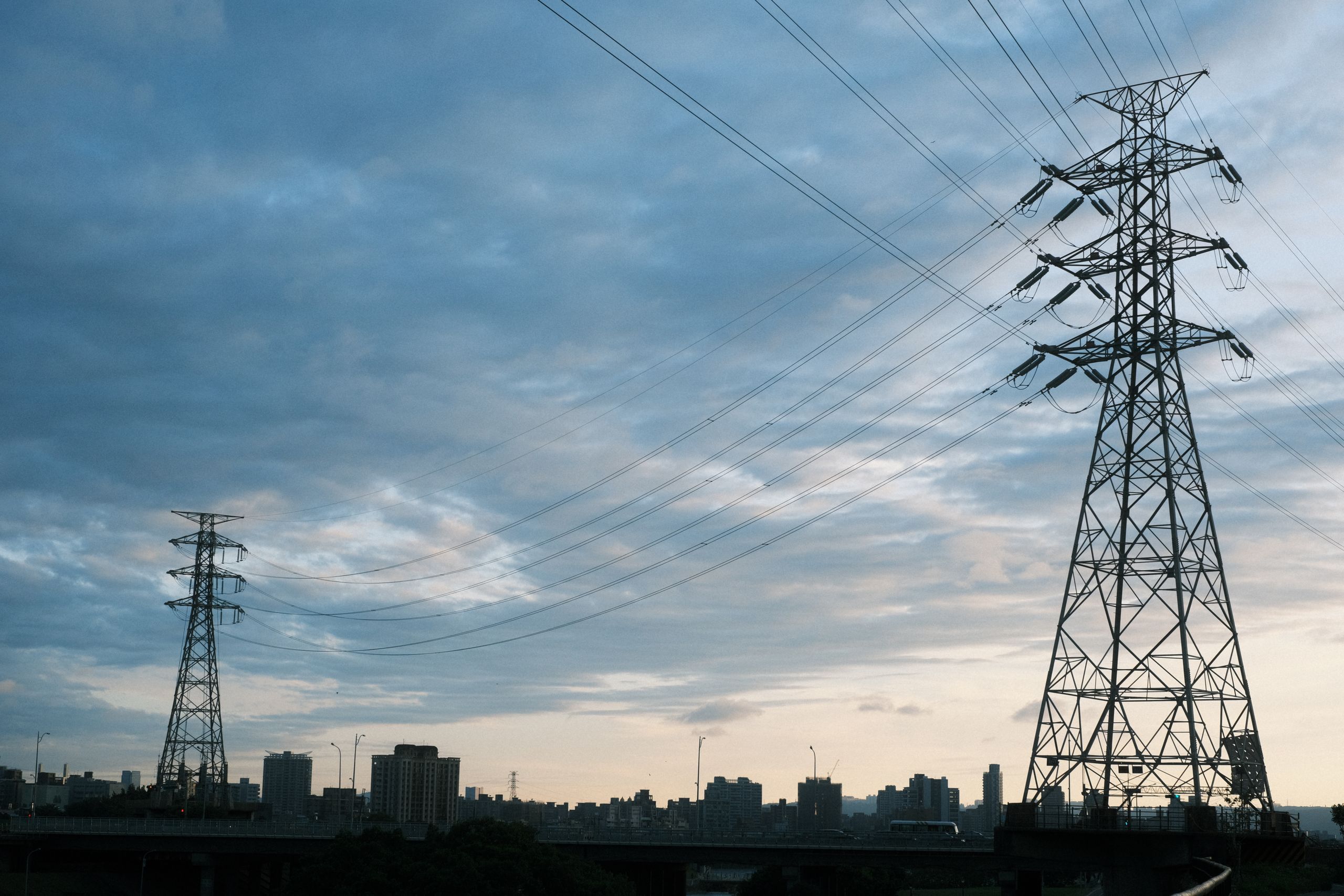 Transmission towers and high-voltage power lines in front of a city skyline at dusk