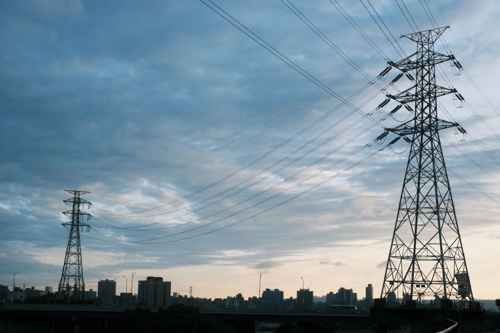 Transmission towers and high-voltage power lines in front of a city skyline at dusk