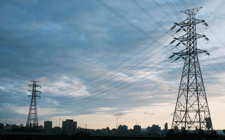 Transmission towers and high-voltage power lines in front of a city skyline at dusk