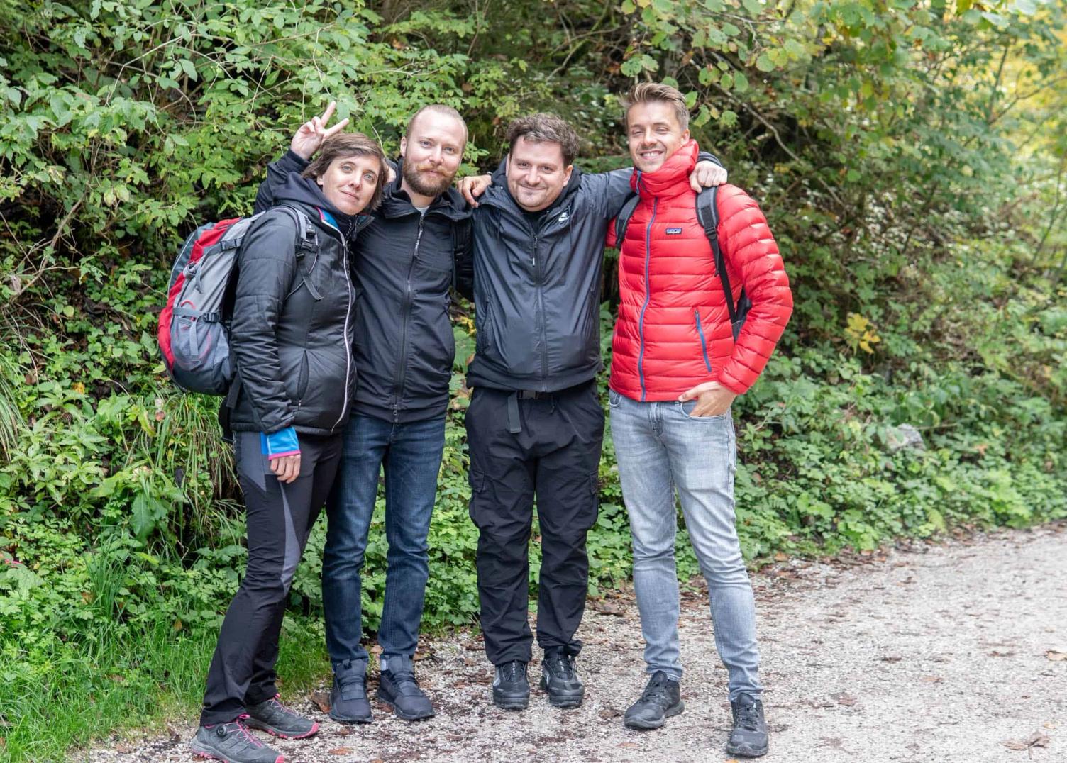 Foto von vier Personen in Outdoor-Jacken, die Arm in Arm auf einem Waldweg stehen