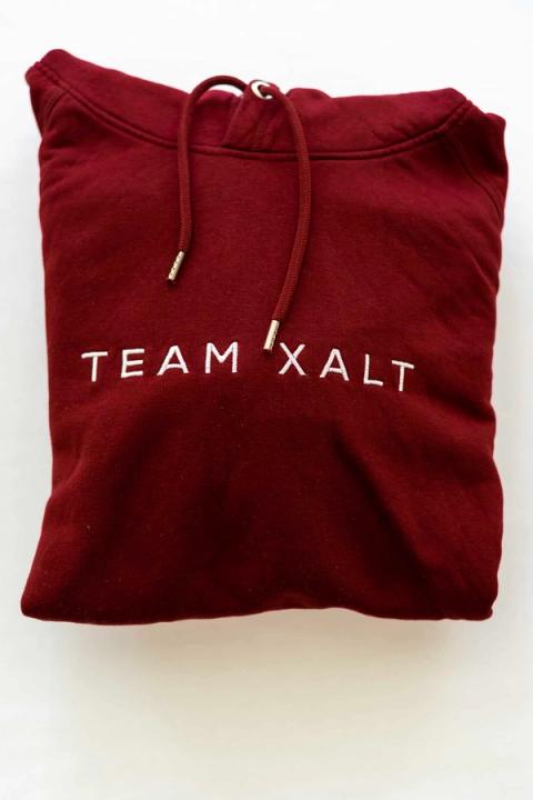 Eine dunkelrote Kapuzenjacke mit weißer TEAM-XALT-Stickerei
