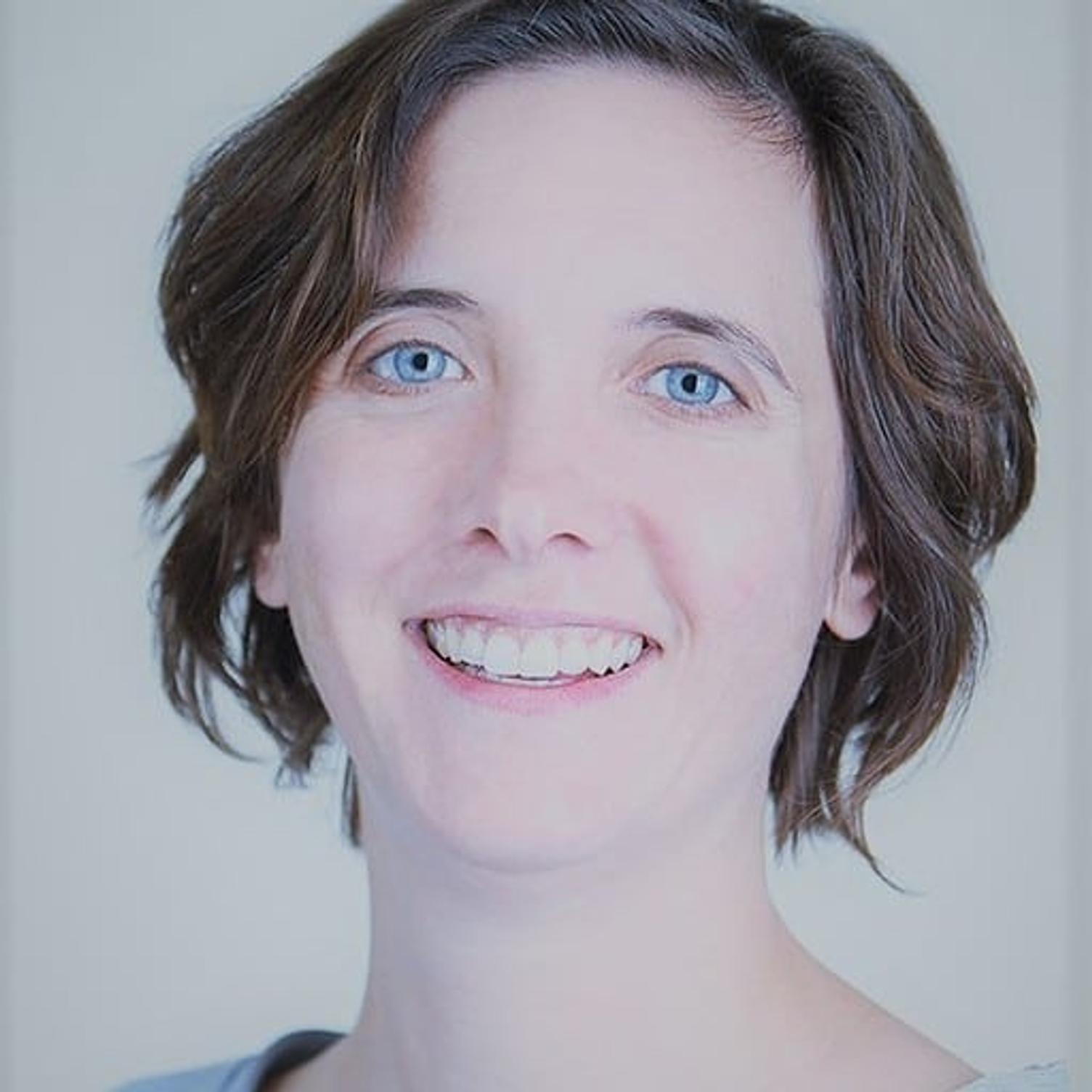 Porträtfoto einer lächelnden Frau mit kurzen braunen Haaren vor hellem Hintergrund