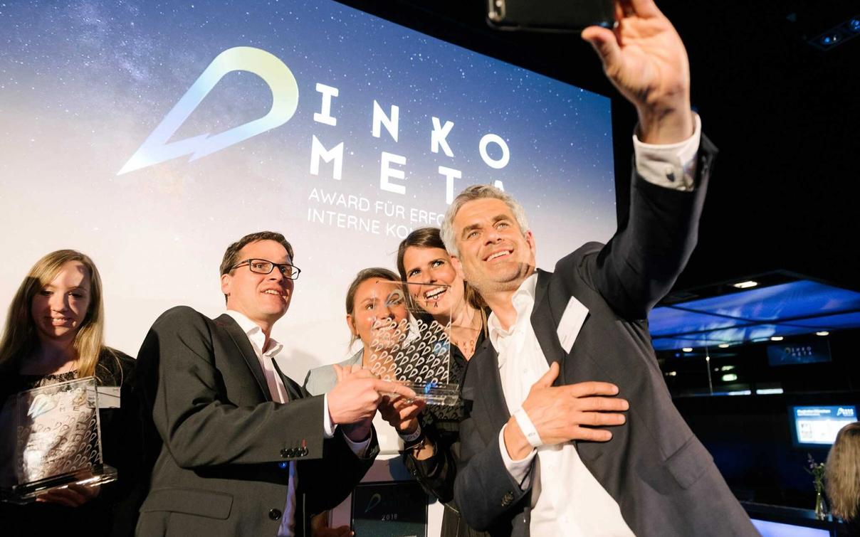 XALT team at the DINKOMETA Awards with trophy, background showing DINKOMETA logo and award banner.