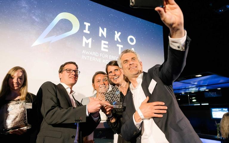 XALT-Team bei der DINKOMETA Award-Verleihung mit Trophäe, Hintergrund: DINKOMETA Logo und Award-Banner.