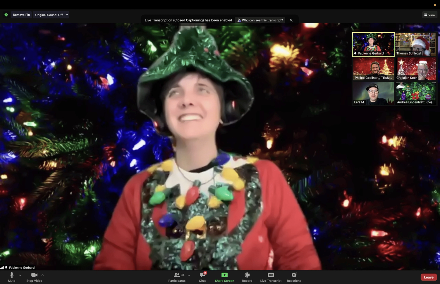 Screenshot einer Zoom-Weihnachtsfeier: eine Teilnehmerin mit Weihnachtsbaum-Hut und Lichterketten-Pullover vor einem geschmückten Baum, rechts weitere Teilnehmende in kleinen Kacheln