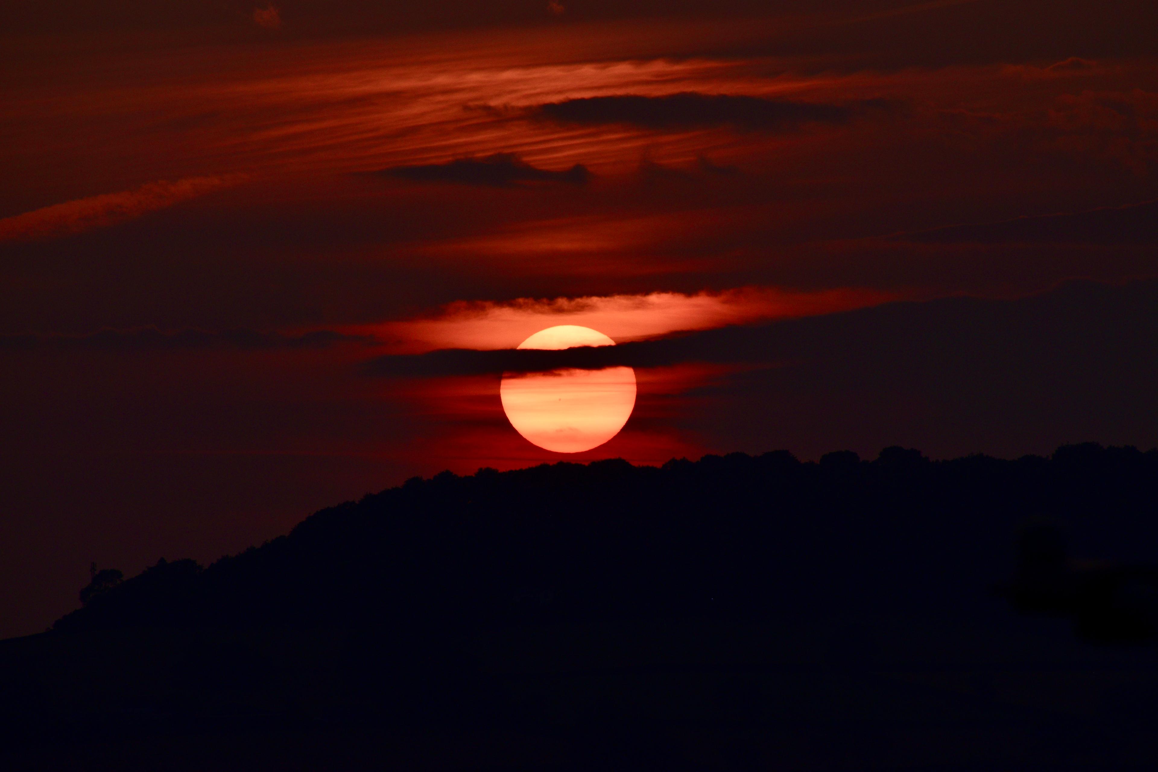 The sun setting behind the hills, caught between two bands of cloud.