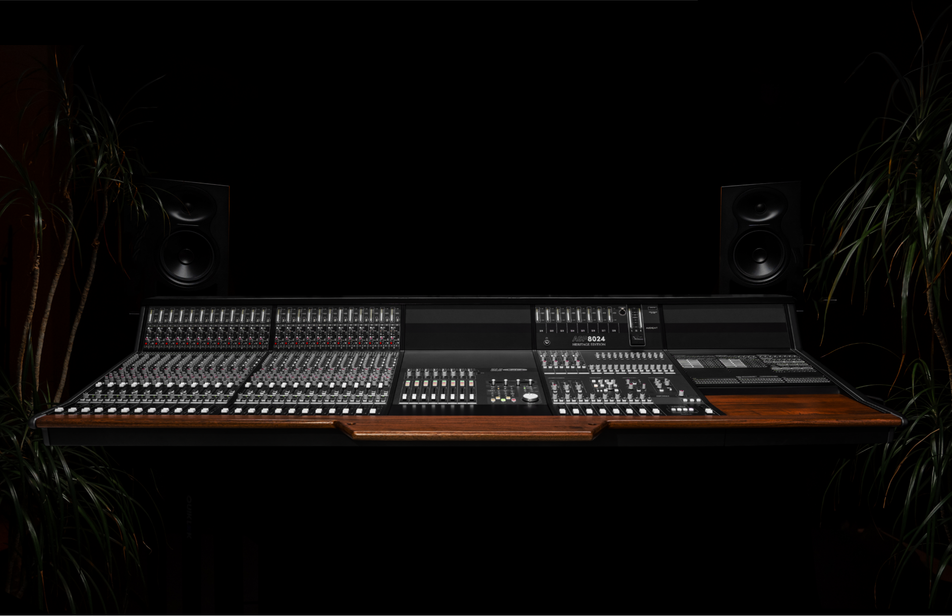 ASP8024 Heritage Edition, full width against a dark studio backdrop — walnut armrest, monitors and plants either side
