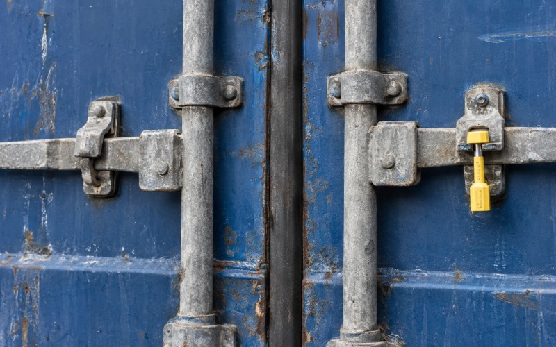 A sealed shipping-container door with locking bars and a numbered cargo seal