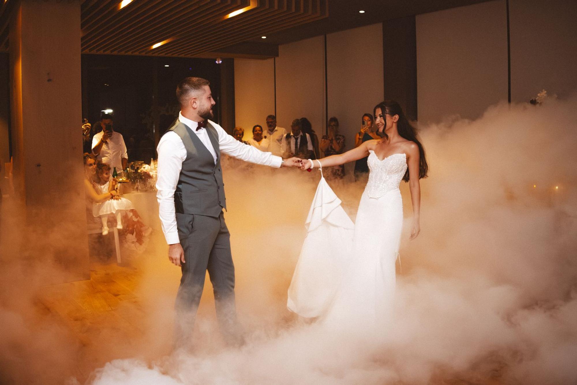 Bride and groom during their first dance in low fog, with guests watching