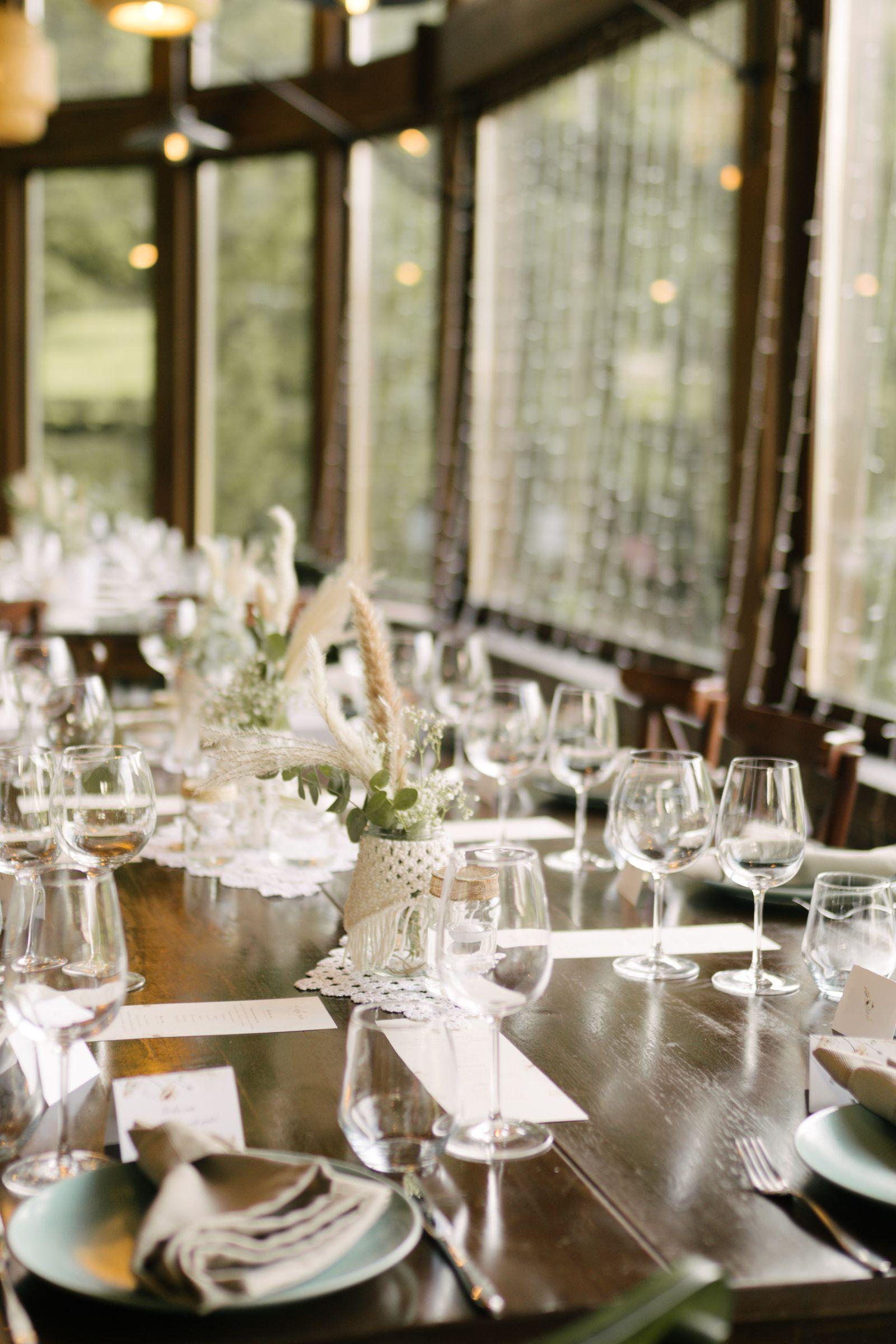 Wedding table set with glasses, plates and dried-flower decorations by a large window