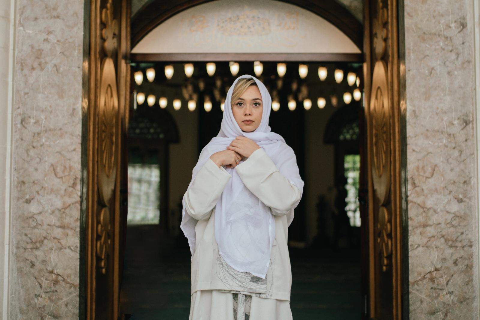 Bride in a white coat and headscarf standing in the doorway of a mosque