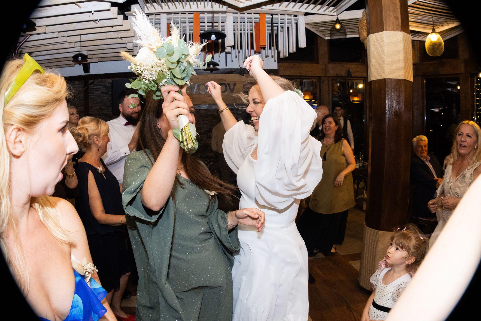 Bride dancing with her guests while one of them holds the bouquet up in the air