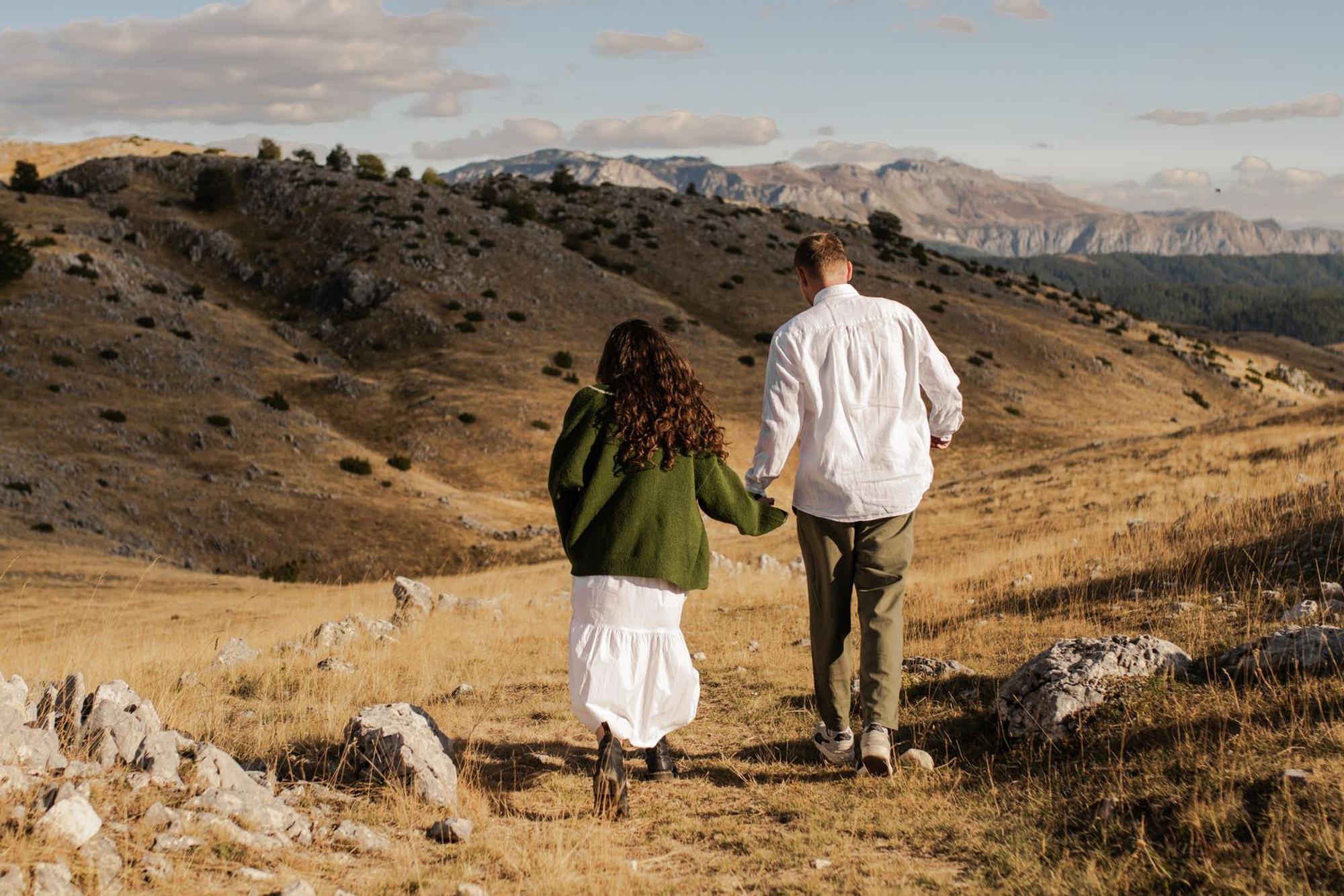 Couple walking hand in hand across golden highlands with mountains in the distance