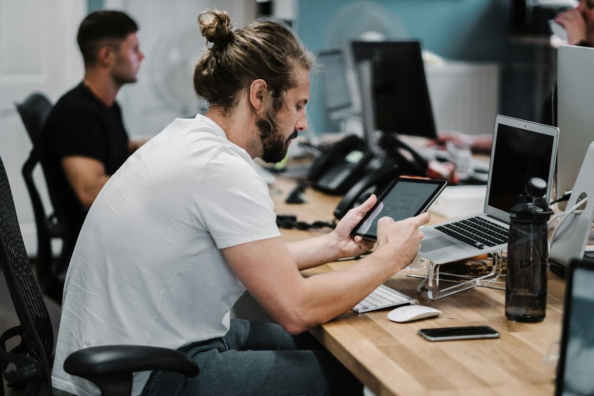 A man using a tablet at his desk in a busy open-plan office