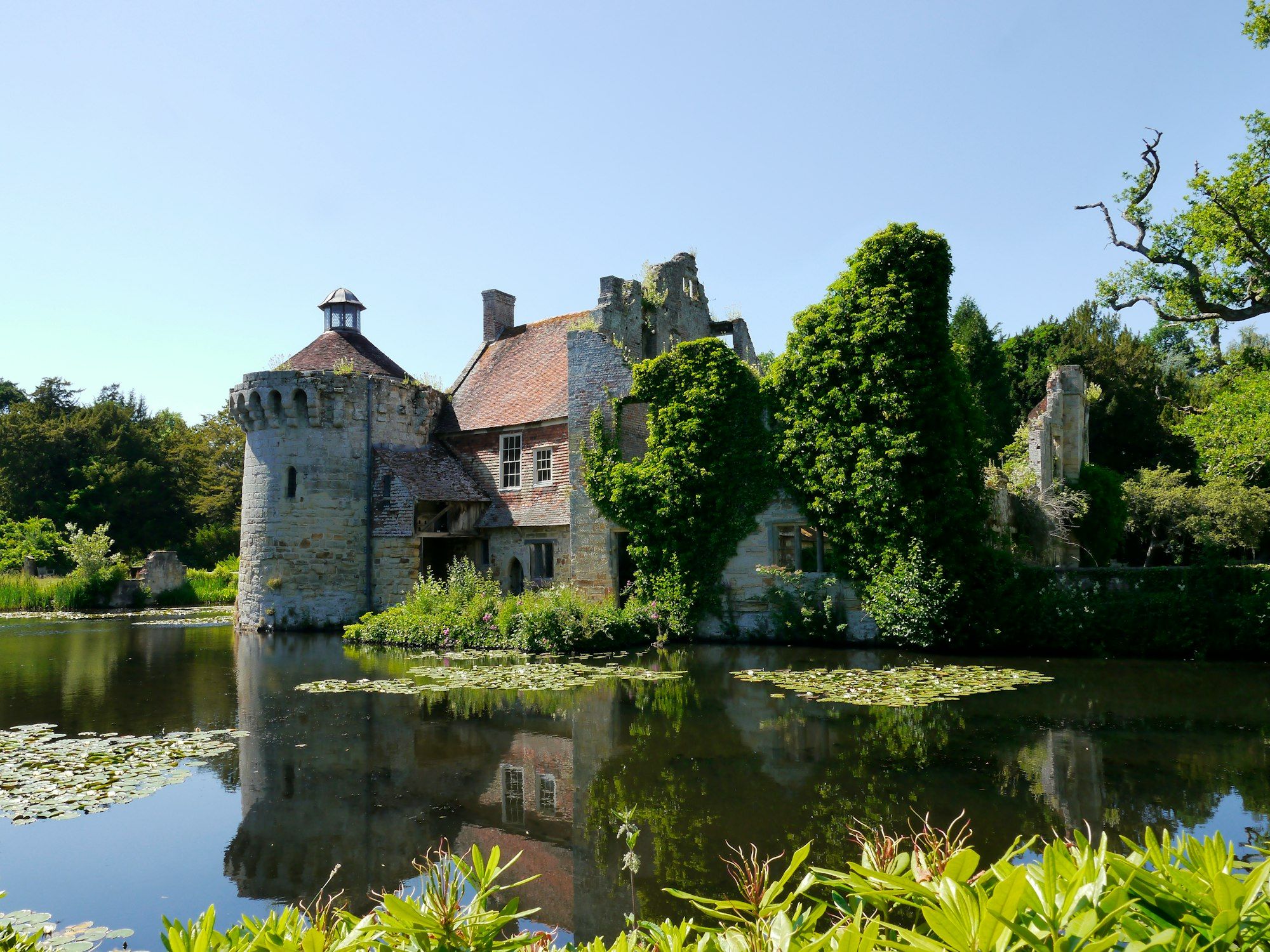 Ivy-covered stone manor house and tower beside a moat, surrounded by trees