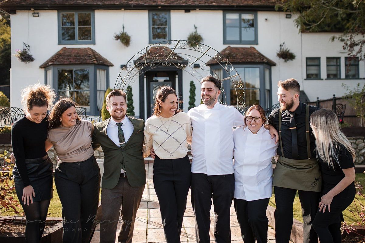 The Orchard team posing together outside the venue's entrance with its wedding arch