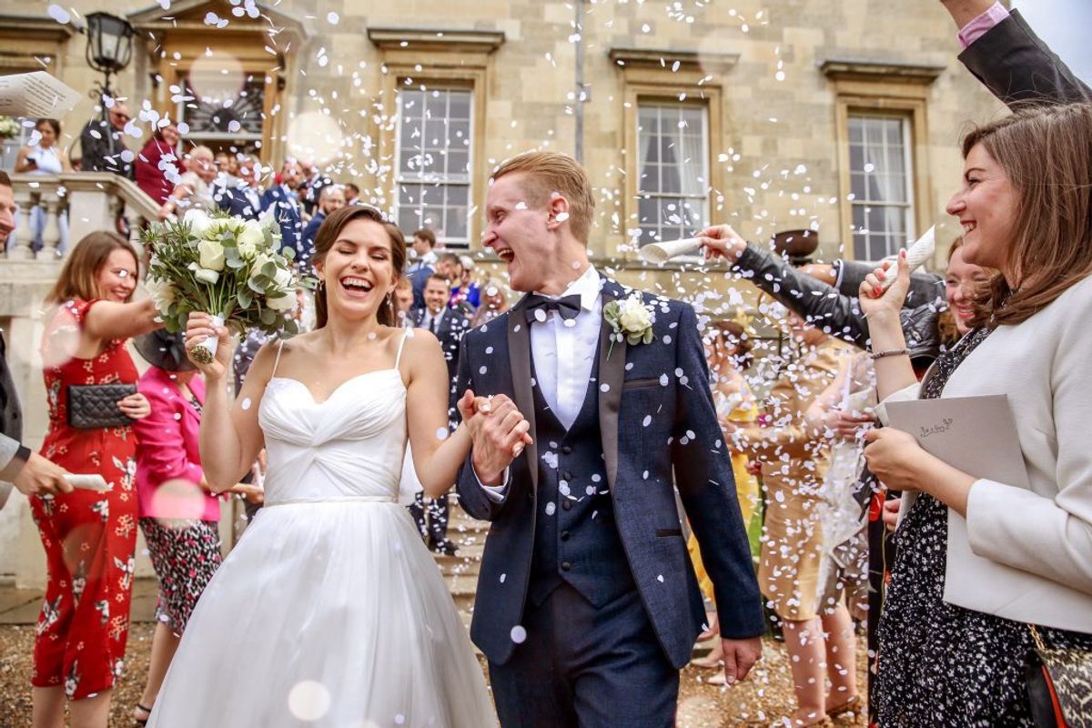 Bride and groom laughing under a shower of confetti outside Harper Weddings