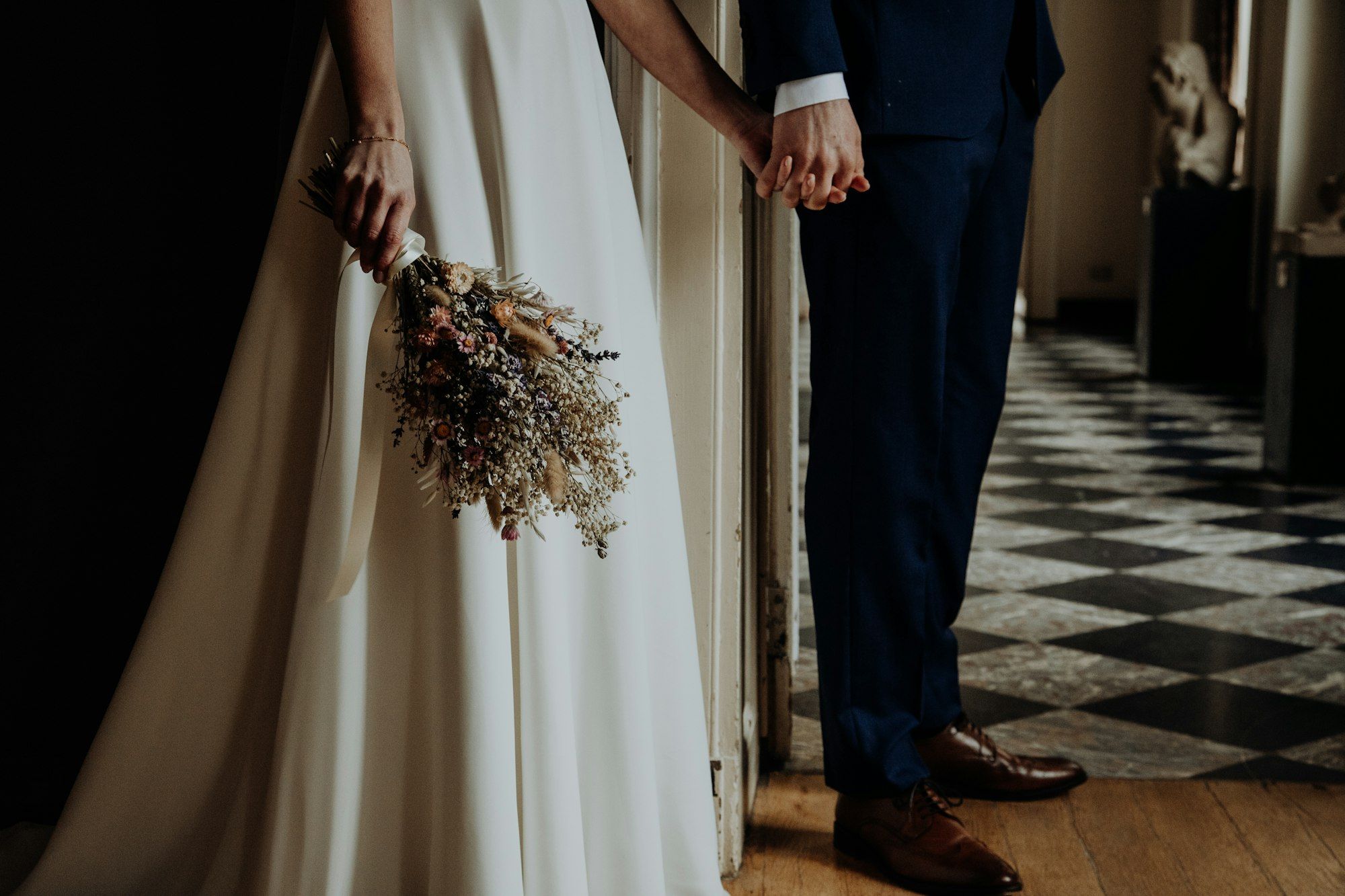 Bride and groom holding hands beside a dried flower wedding bouquet