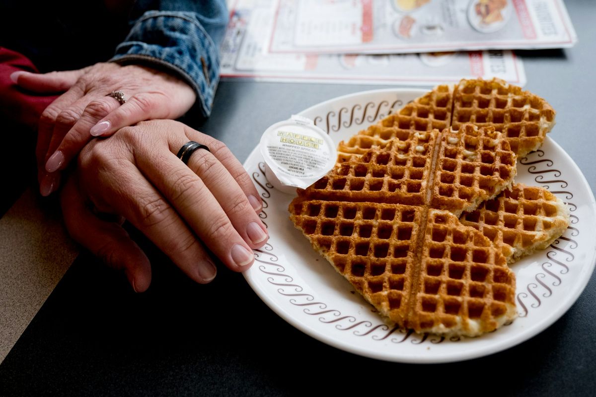 Two hands wearing wedding rings beside a plate of waffles